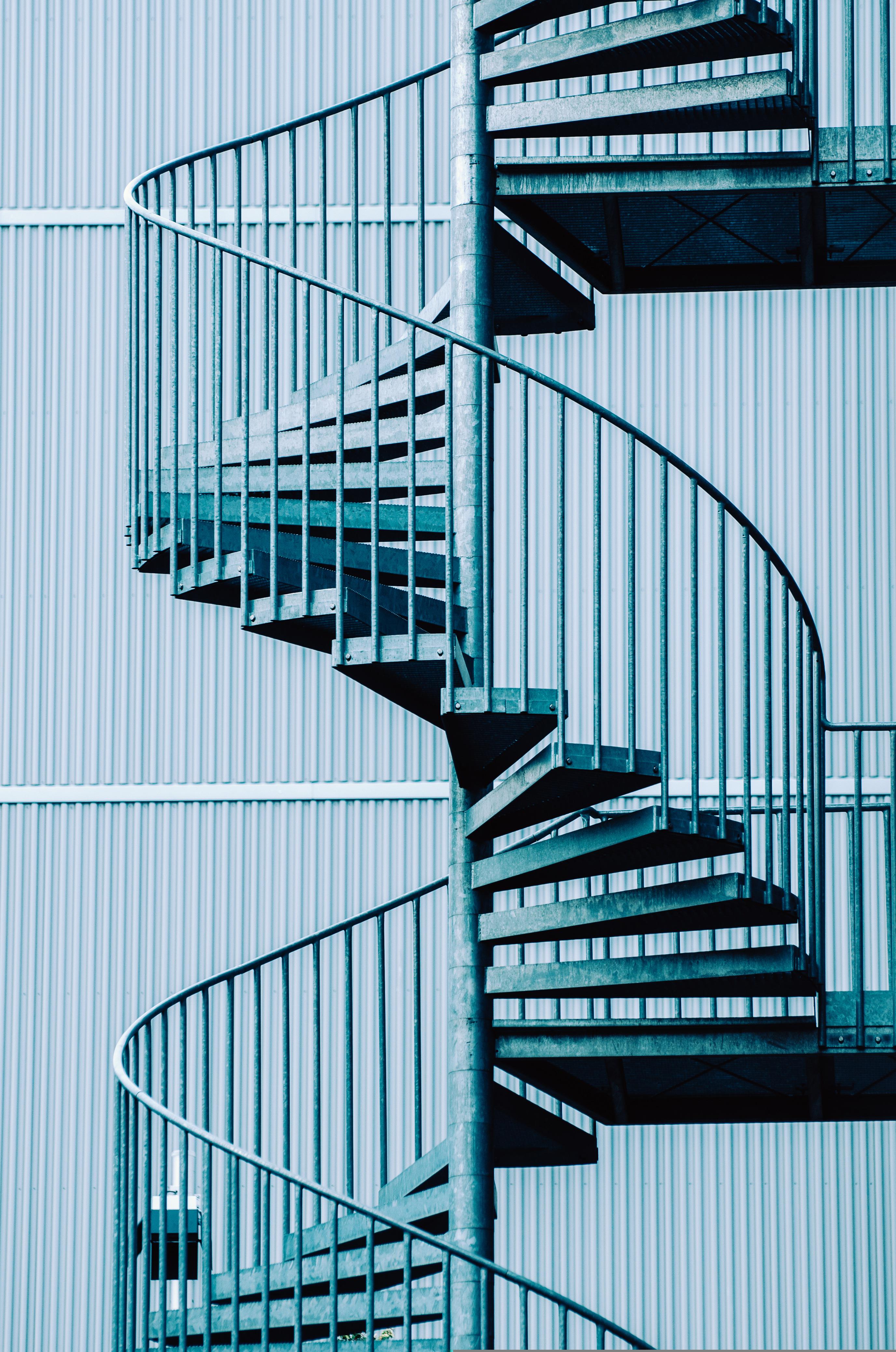 Escalier en colimaçon compact en acier reliant deux niveaux près d’un mur industriel